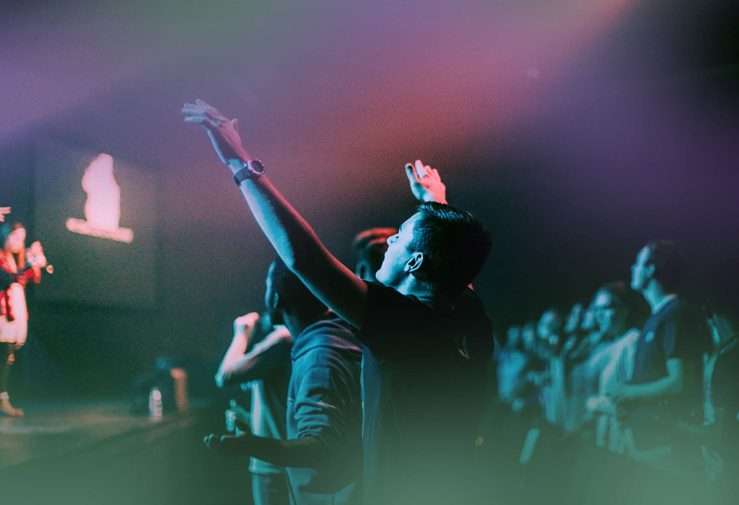 People worshiping at House of Judah event with raised hands and vibrant lighting.