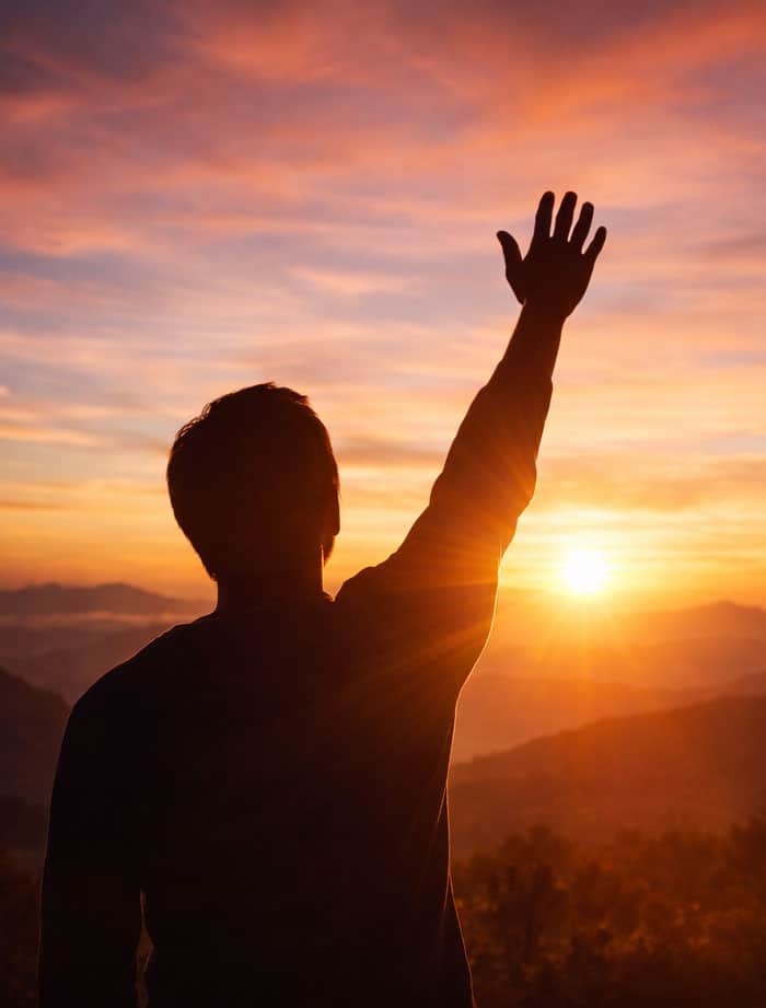 silhouette of male raising hand in worship at sunset